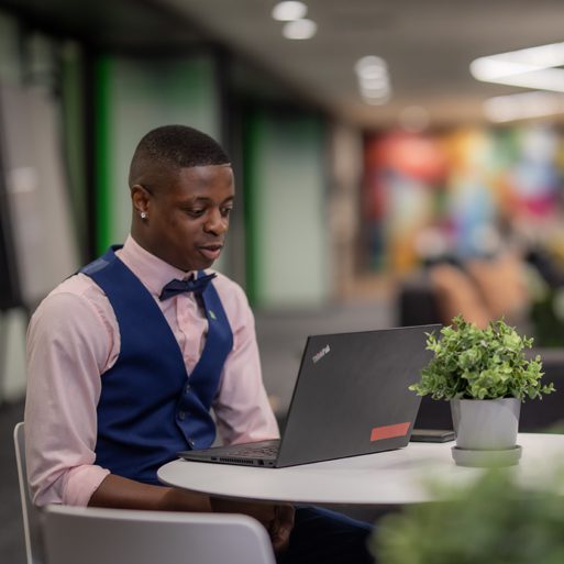 A child sits on their parent’s shoulders while they work from a laptop at their kitchen table.