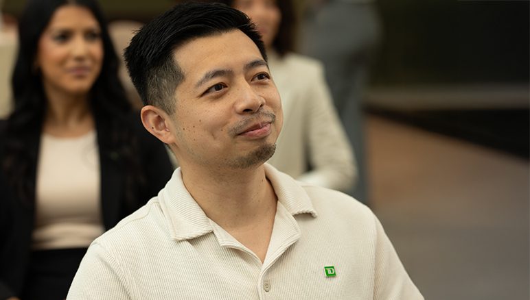 A new colleague smiles in front of a whiteboard inside a TD office.