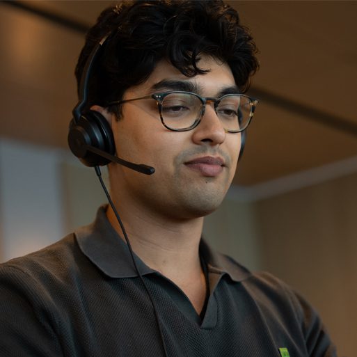 A contact centre colleague wearing a headset and TD name tag smiles at their desk.