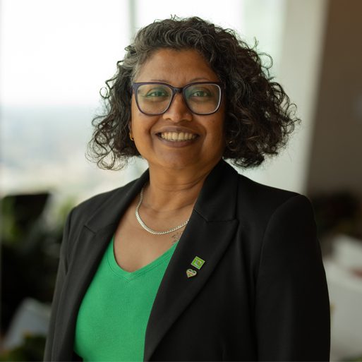 A colleague wearing a hijab and a green TD lapel pin smiles in an office.