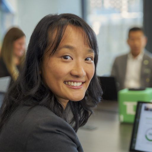 Two colleagues smile while working together in front of a computer.